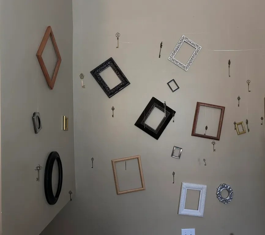 A wall featuring various picture frames of different shapes and sizes, some hanging from strings along with vintage keys.